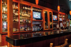 A bar with shelves of liquor bottles and a television screen displaying a news program. - Holiday Inn Pewaukee - Milwaukee West by IHG (Pewaukee)