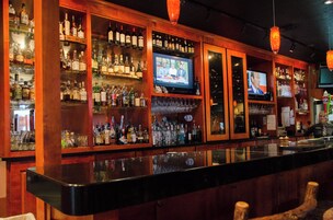 Un bar con estantes llenos de botellas de licores y una pantalla de televisión mostrando un noticiero.
