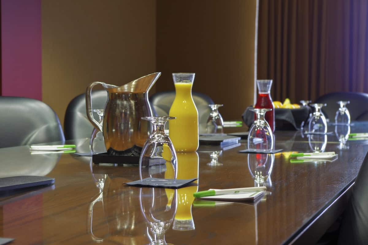 Una mesa de conferencias con varios vasos y una jarra de líquido amarillo, probablemente jugo, en una sala de reuniones.