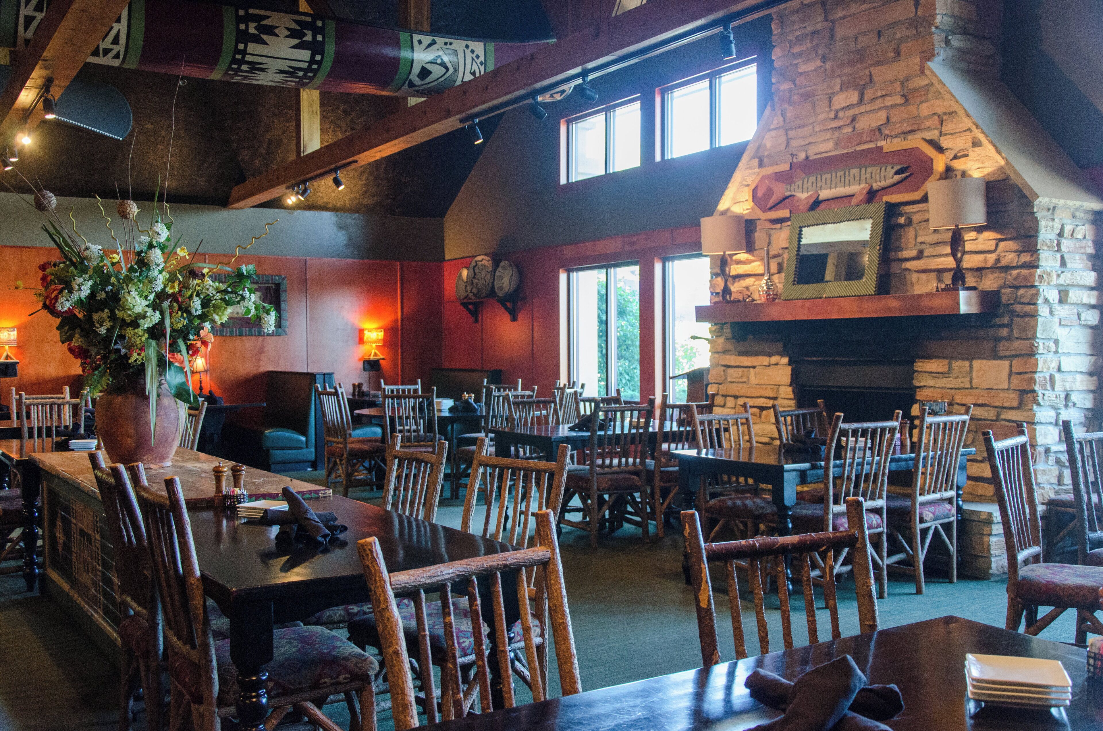 A restaurant with a stone fireplace, wooden tables, and chairs.