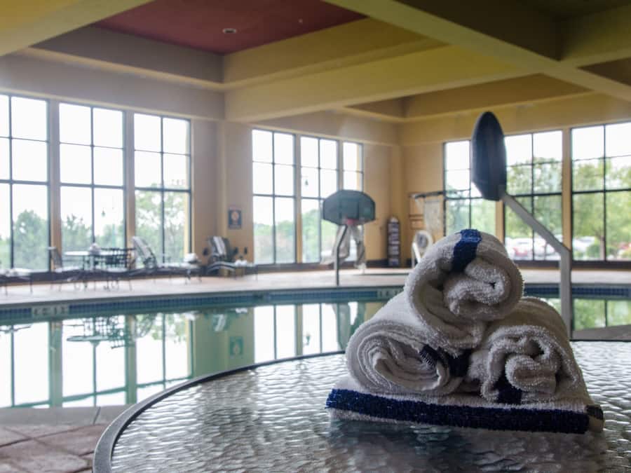 Un área de piscina con mesa de vidrio, sillas de descanso y canasta de baloncesto.