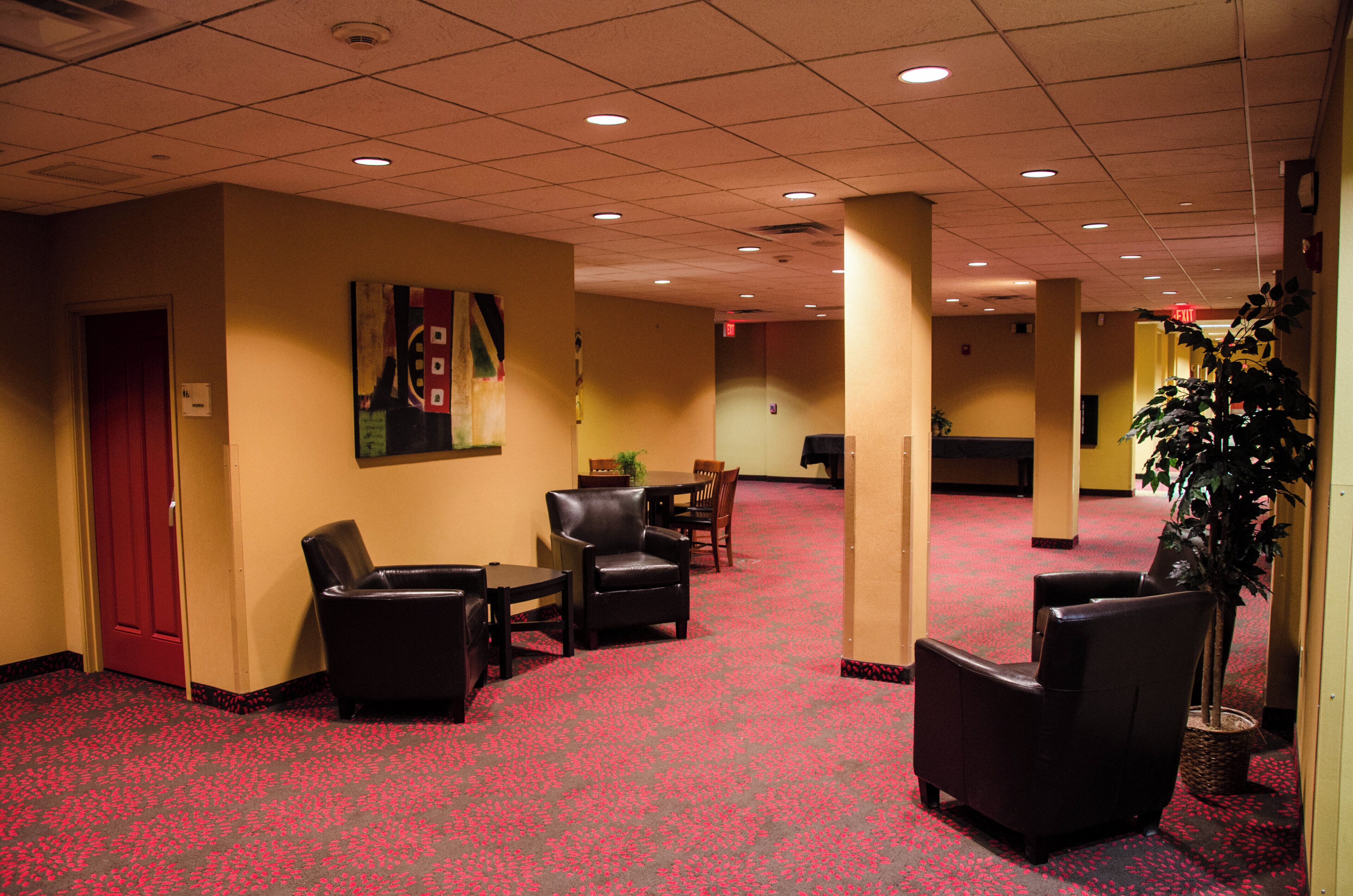 A hotel lobby with a red carpet, leather chairs, a painting on the wall, and a potted plant.