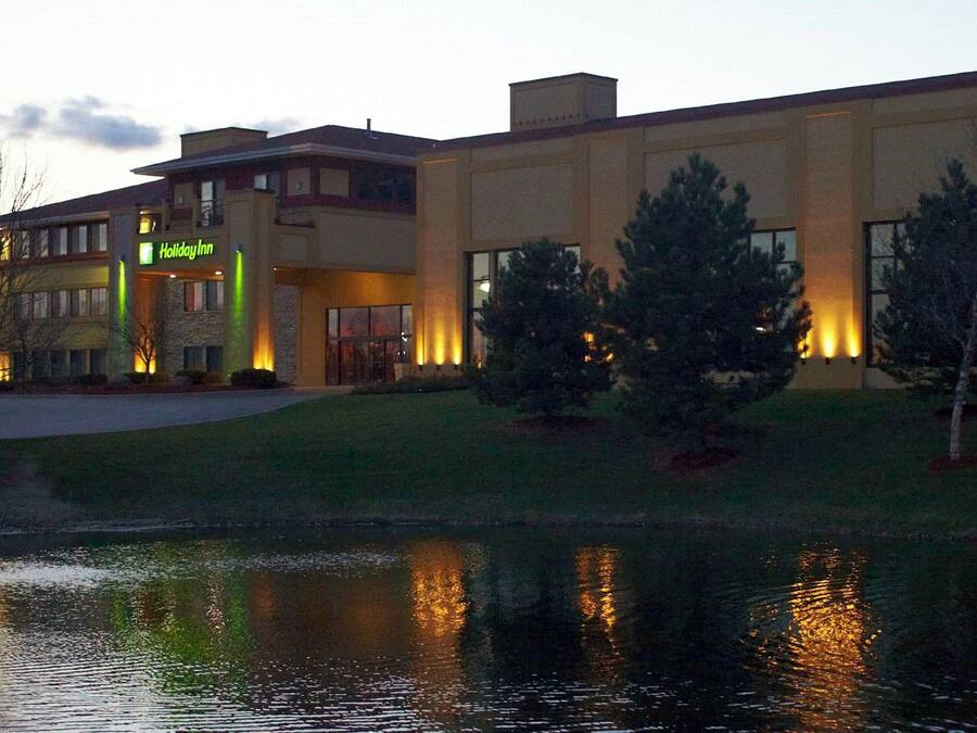 A Holiday Inn hotel with a large building, a pond, and trees in front.