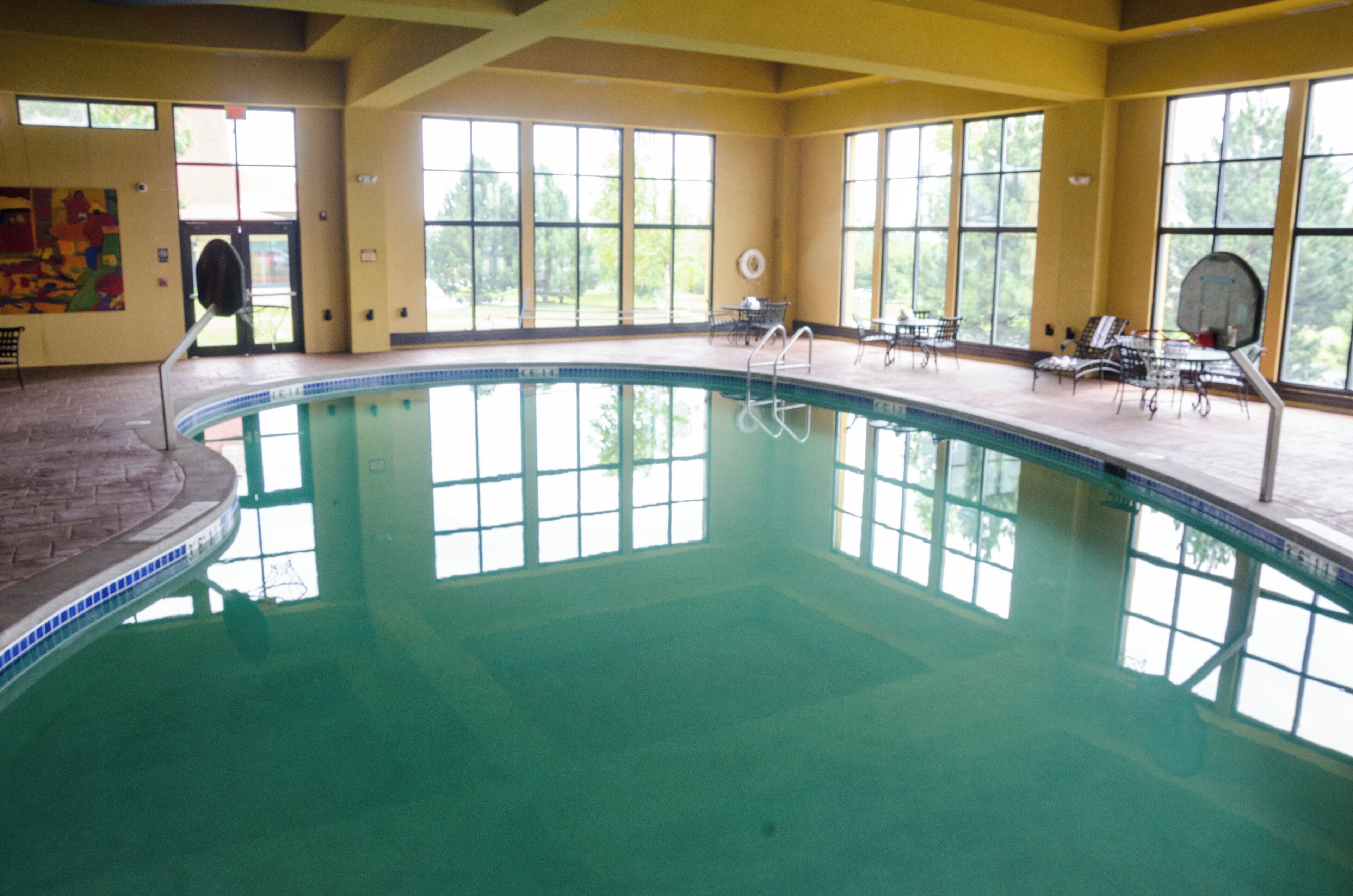 An indoor swimming pool with clear glass walls, a tiled deck, and lounge chairs.