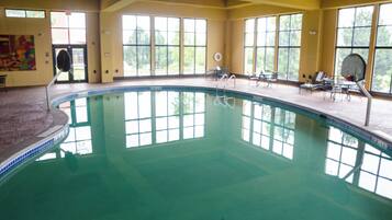 An indoor swimming pool with clear glass walls, a tiled deck, and lounge chairs.