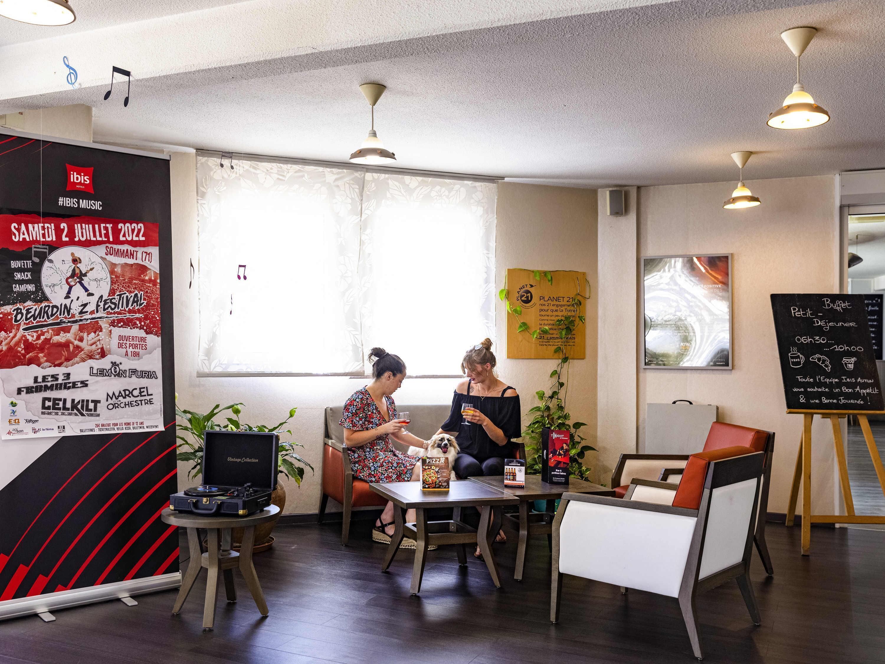 A cozy indoor setting with a poster advertising an event, a table with a laptop and a beverage, and a seating area with a dog.