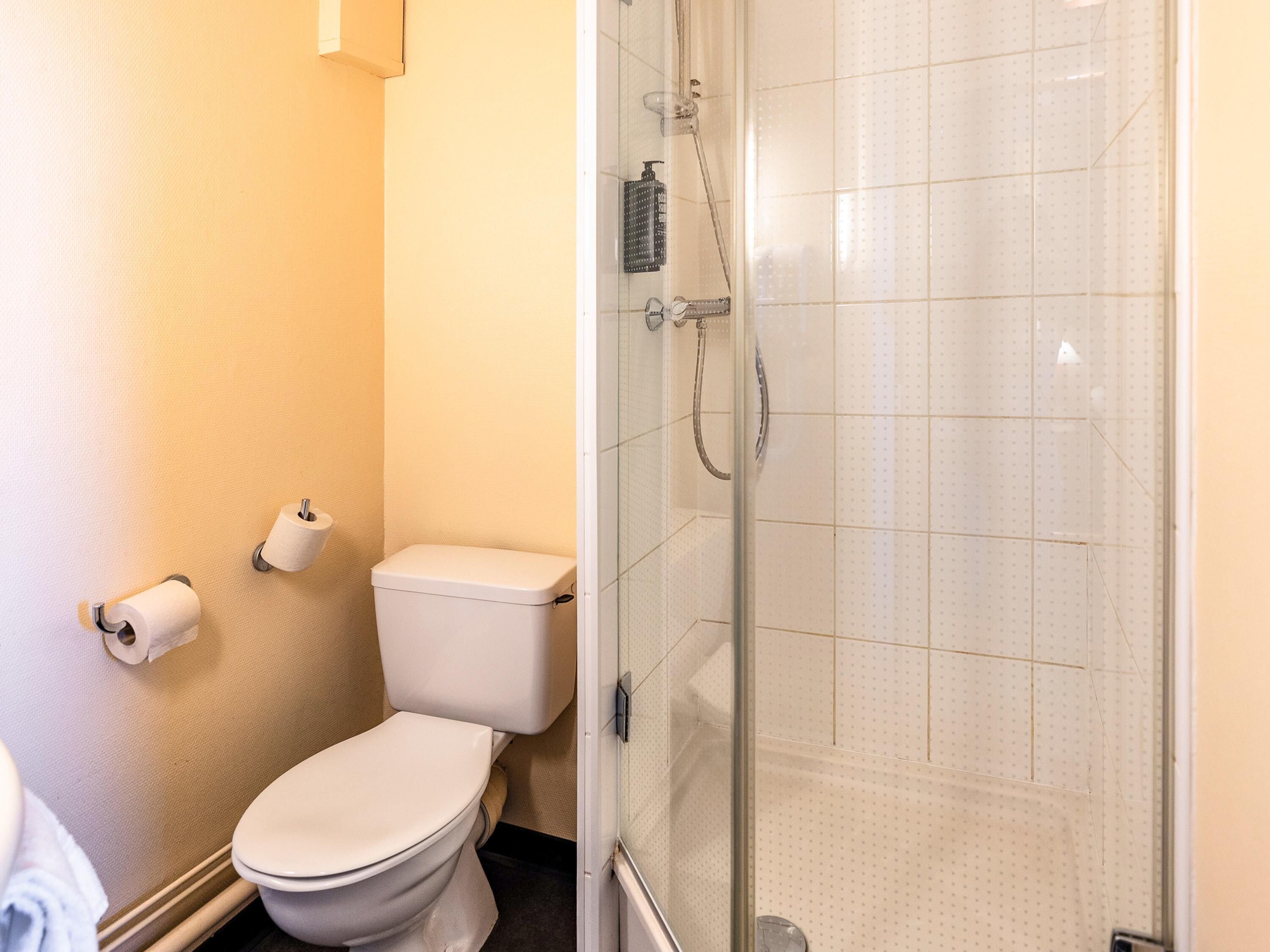 Une salle de bain équipée de toilettes, d’une douche et d’un porte-rouleau de papier toilette.