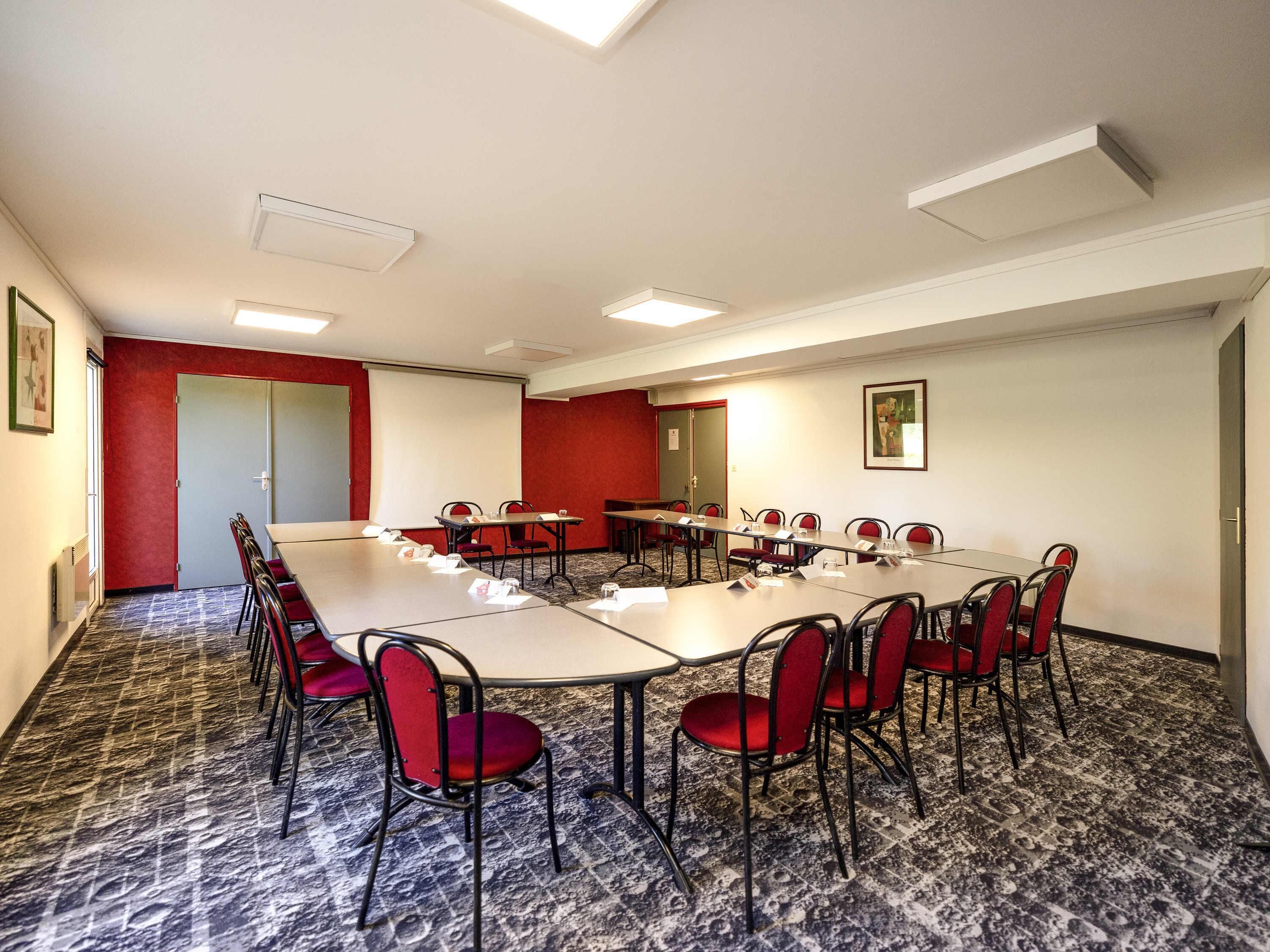 A conference room with a long table, red chairs, and a projector screen.