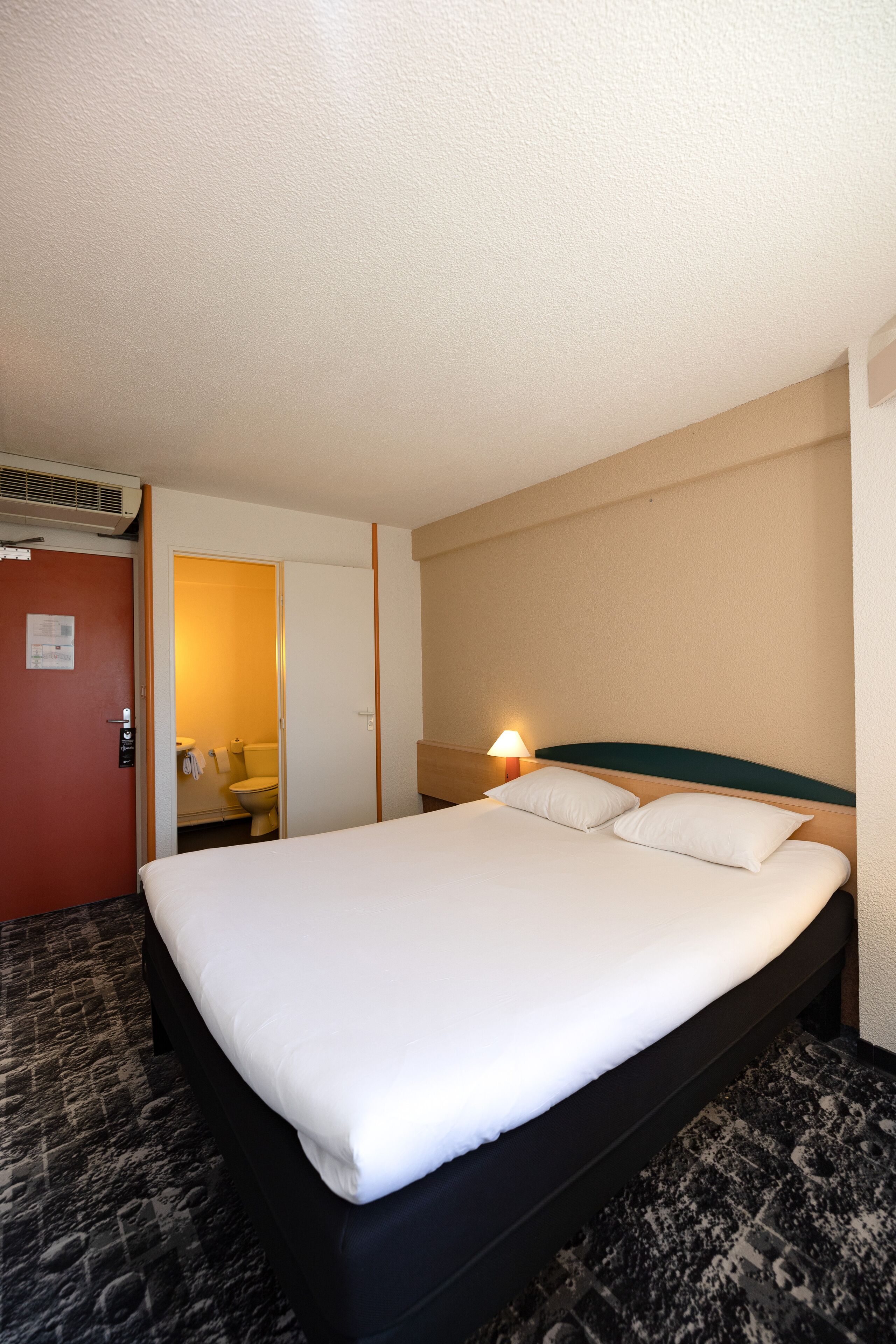 A hotel room with a bed, a bathroom, and a door.