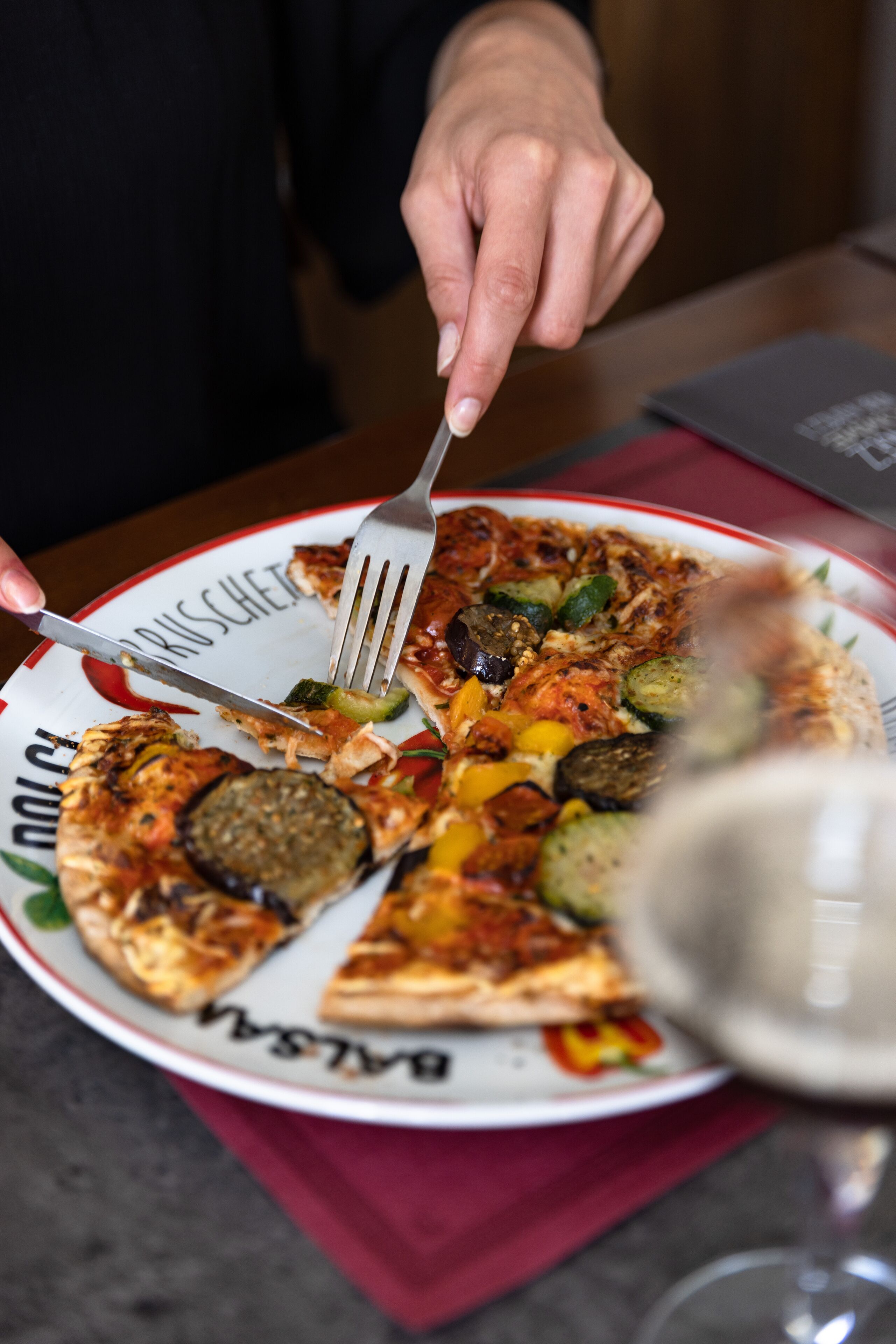 Una persona cortando una pizza con diferentes ingredientes en un plato.