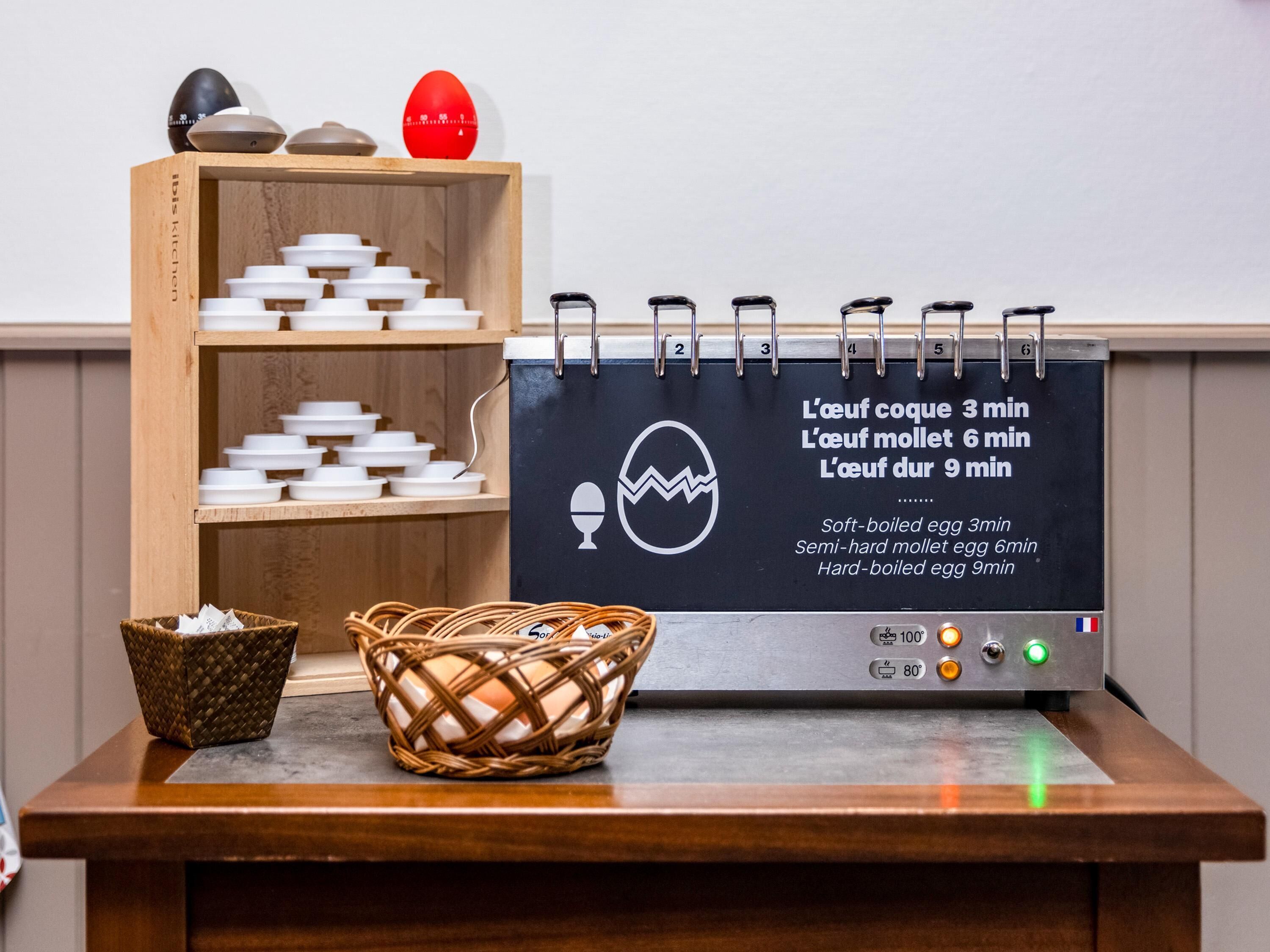 A kitchen area with a wooden shelf holding white bowls, a basket with eggs, and a blackboard with cooking times for eggs.