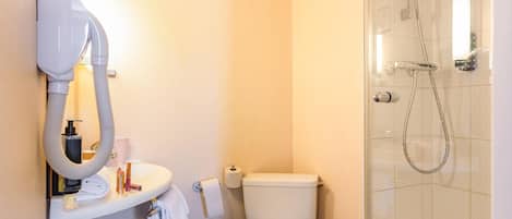 Une salle de bain avec des toilettes blanches, un lavabo équipé d’un sèche-cheveux et un espace douche.