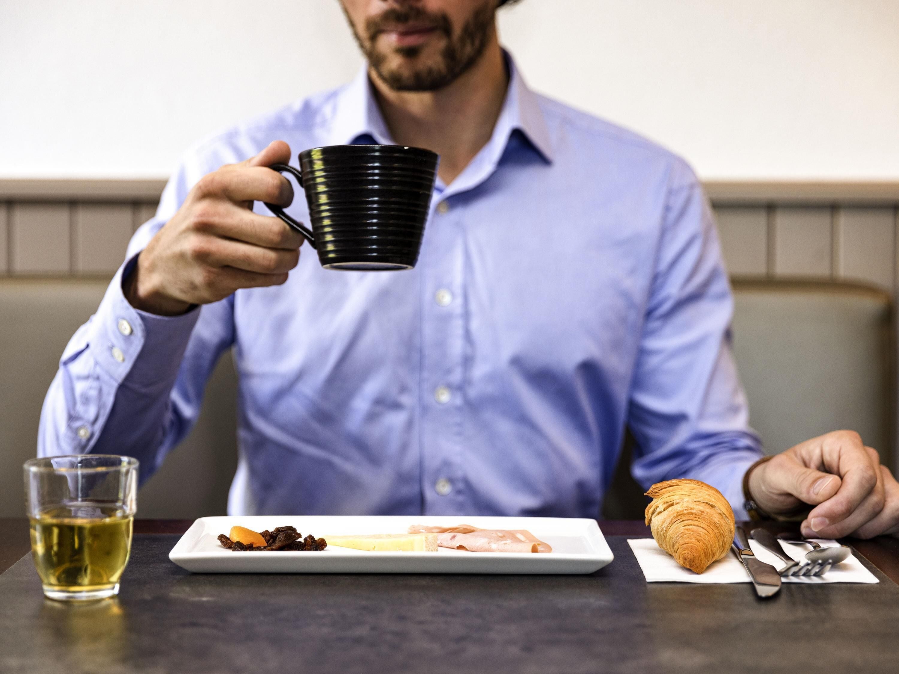 A person sitting at a table with a plate of food, a glass of liquid, and a croissant.