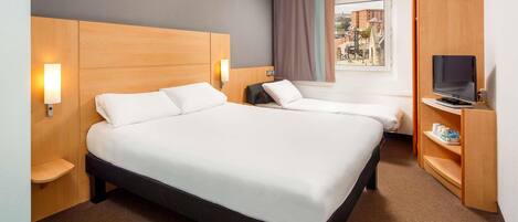 Hotelkamer met een groot bed, nachtkastjes, een televisie op een standaard en uitzicht op de stad door het raam.