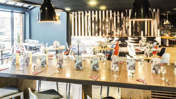 A modern restaurant interior with a long bar, multiple tables, and chairs.