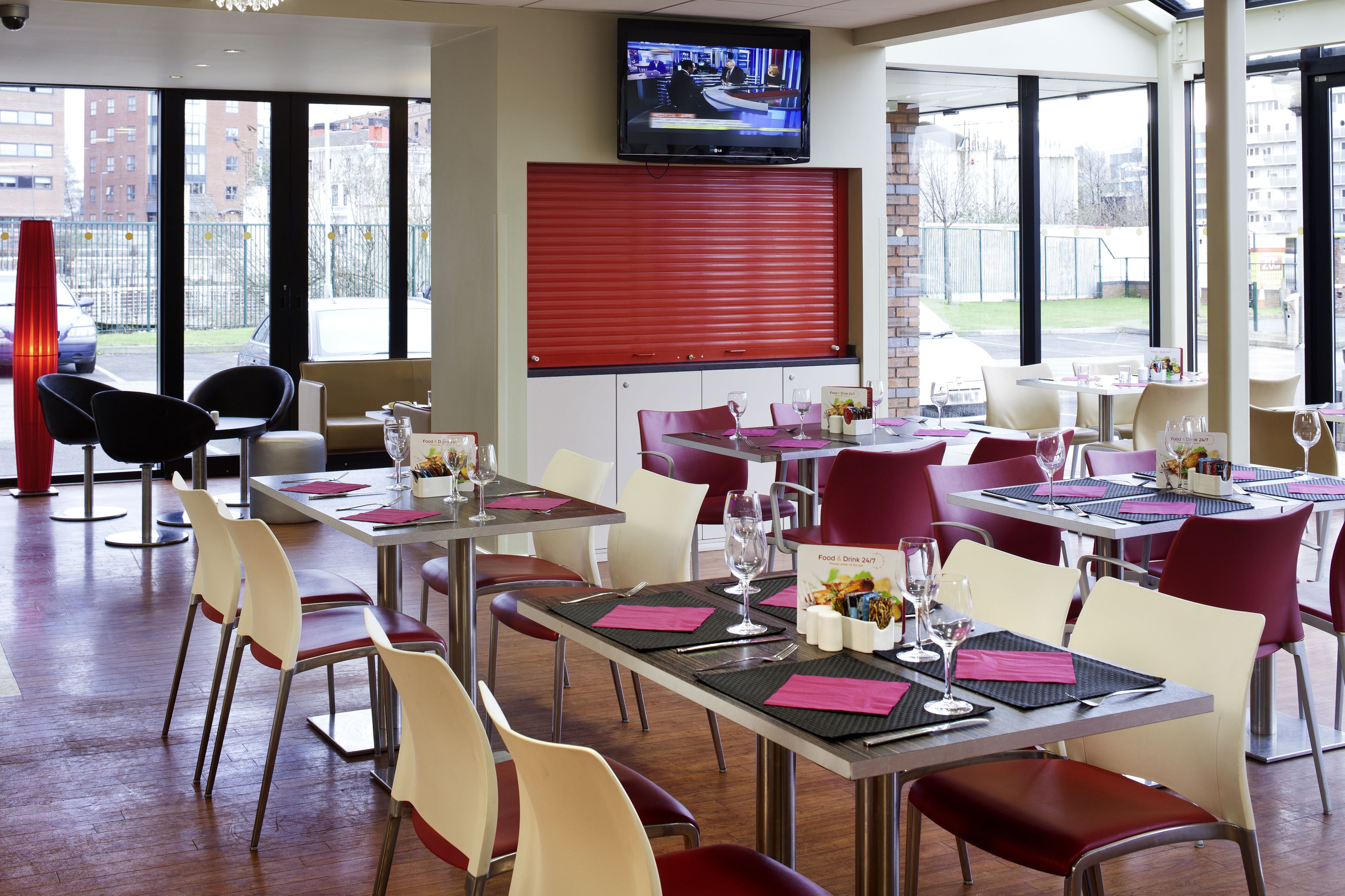 A restaurant with tables set for dining, a TV mounted on the wall, and large windows offering a view of the outside.