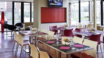 A restaurant with tables set for dining, a TV mounted on the wall, and large windows offering a view of the outside.