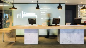 A reception desk with three monitors, a glass wall with a projection of room rates and services, and pendant lighting.