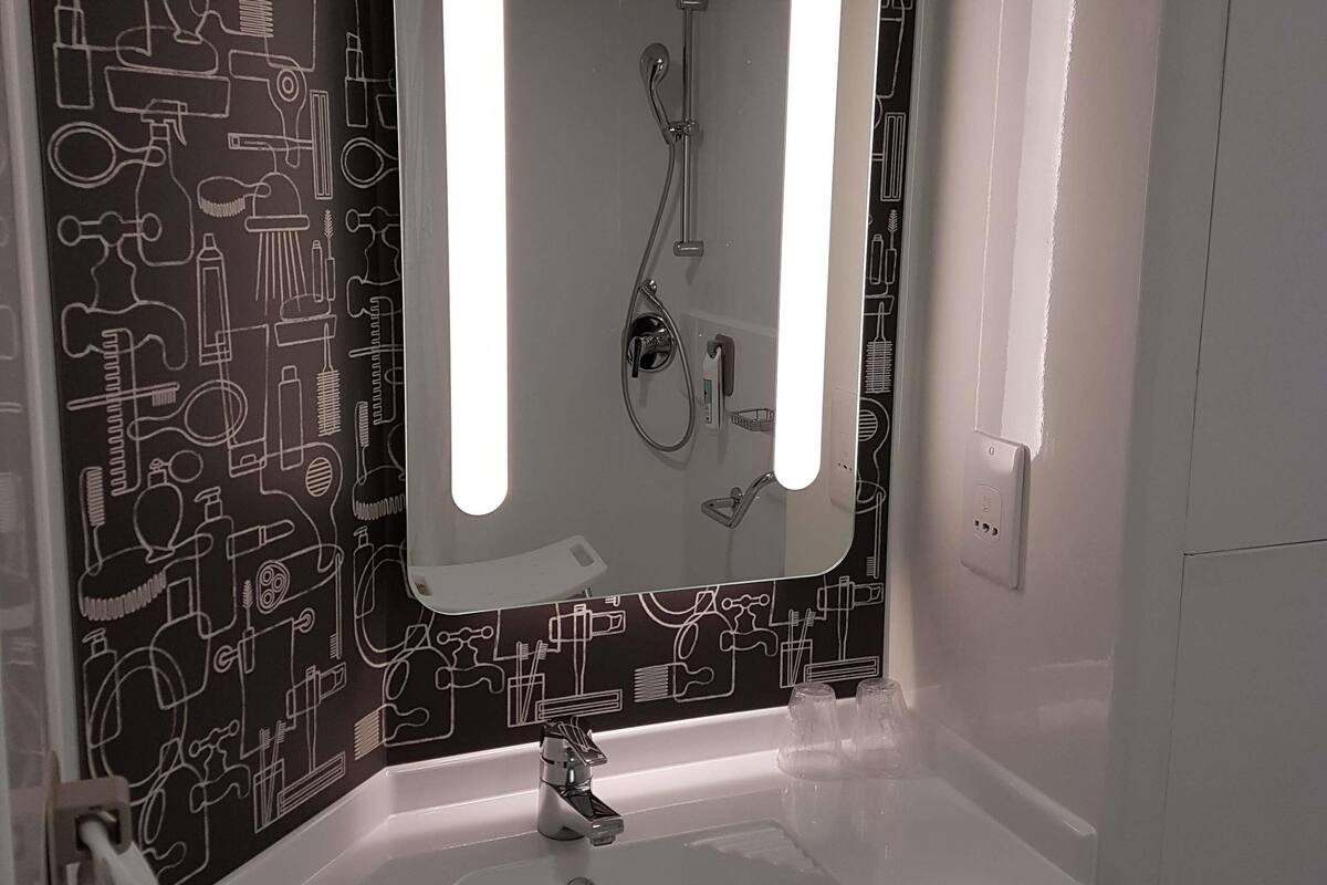 Une salle de bain avec un lavabo, un miroir et une douche. Le mur est décoré d’un motif noir et blanc.