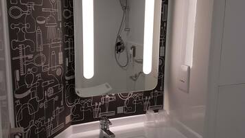 A bathroom with a sink, mirror, and shower. The wall has a black and white pattern.