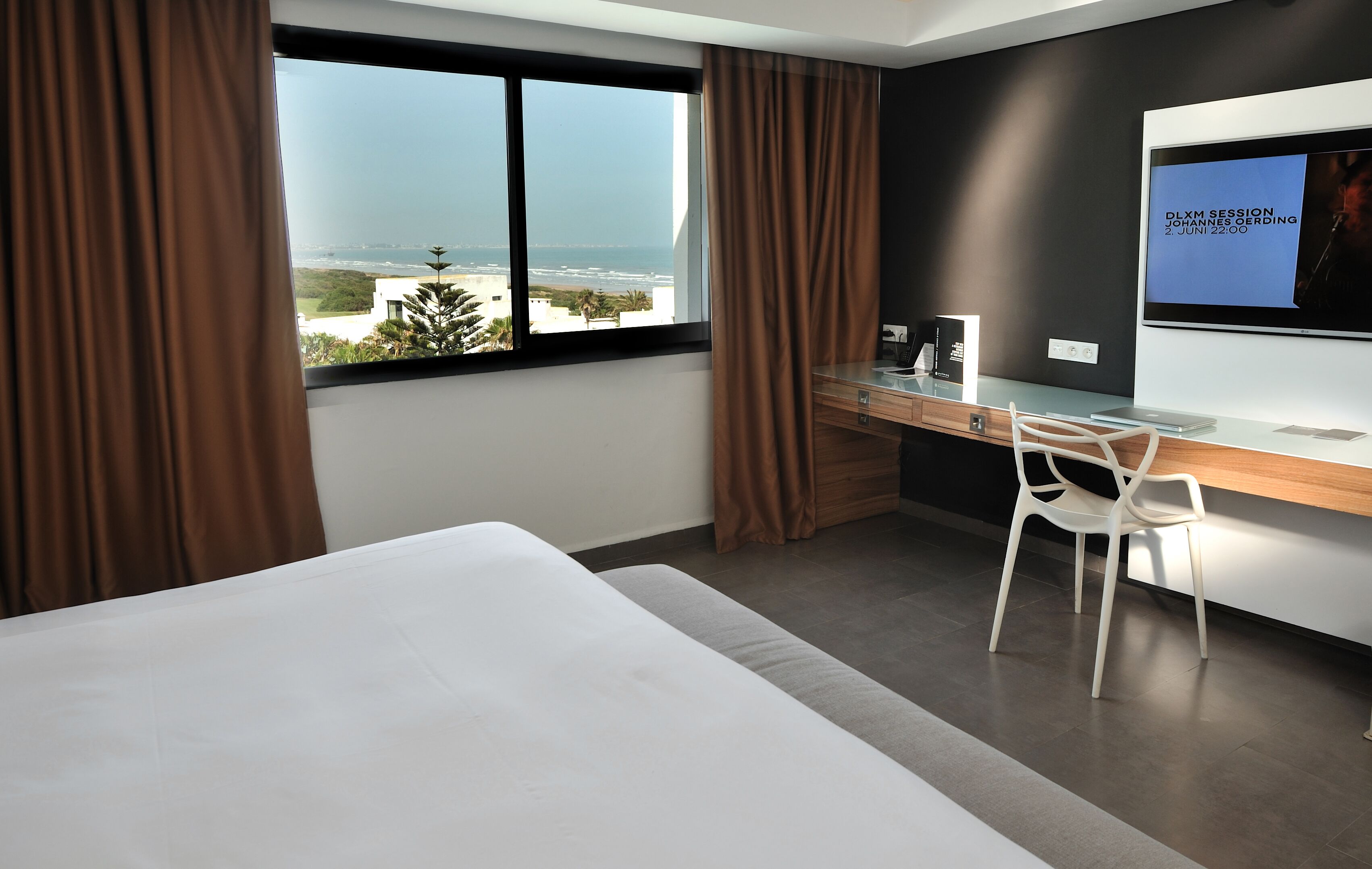 Habitación de hotel moderna con una cama grande, un escritorio y vistas al océano.
