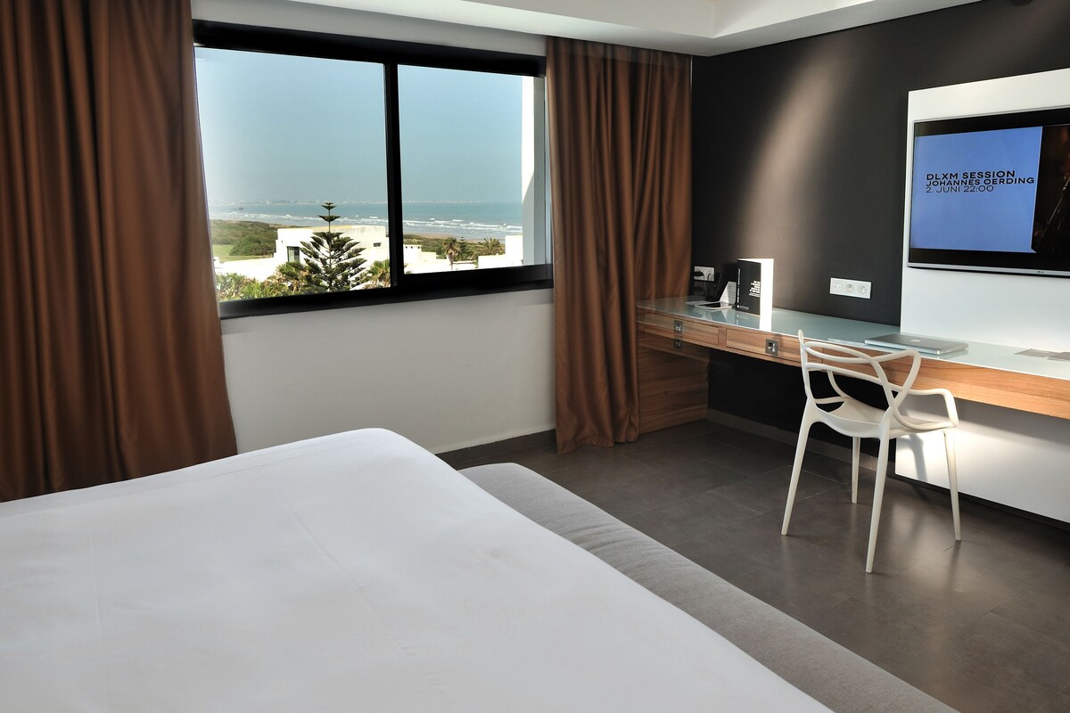 Habitación de hotel moderna con una cama grande, un escritorio y vistas al océano.