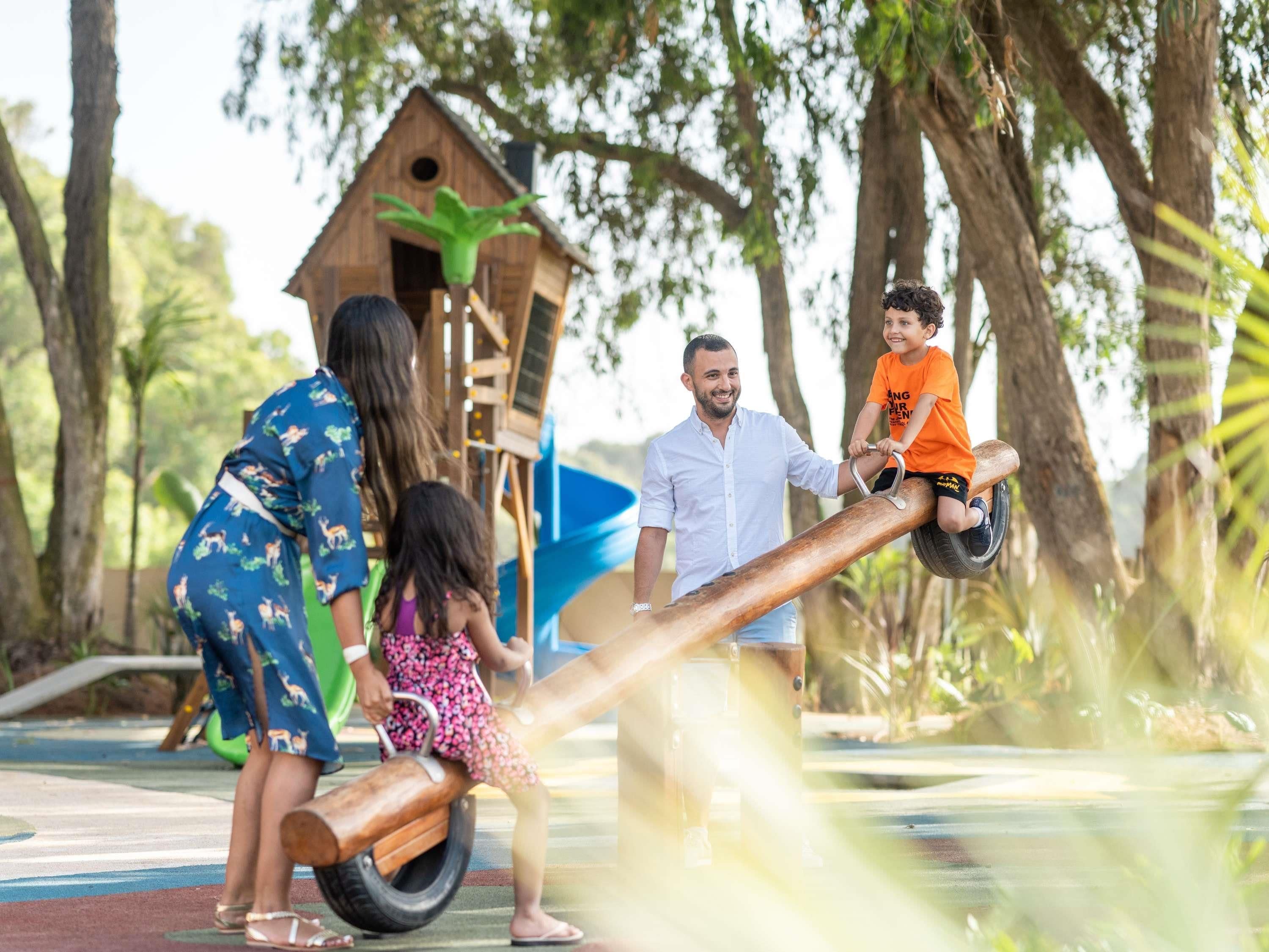 A playground with a seesaw, a wooden structure resembling a birdhouse, and a slide.