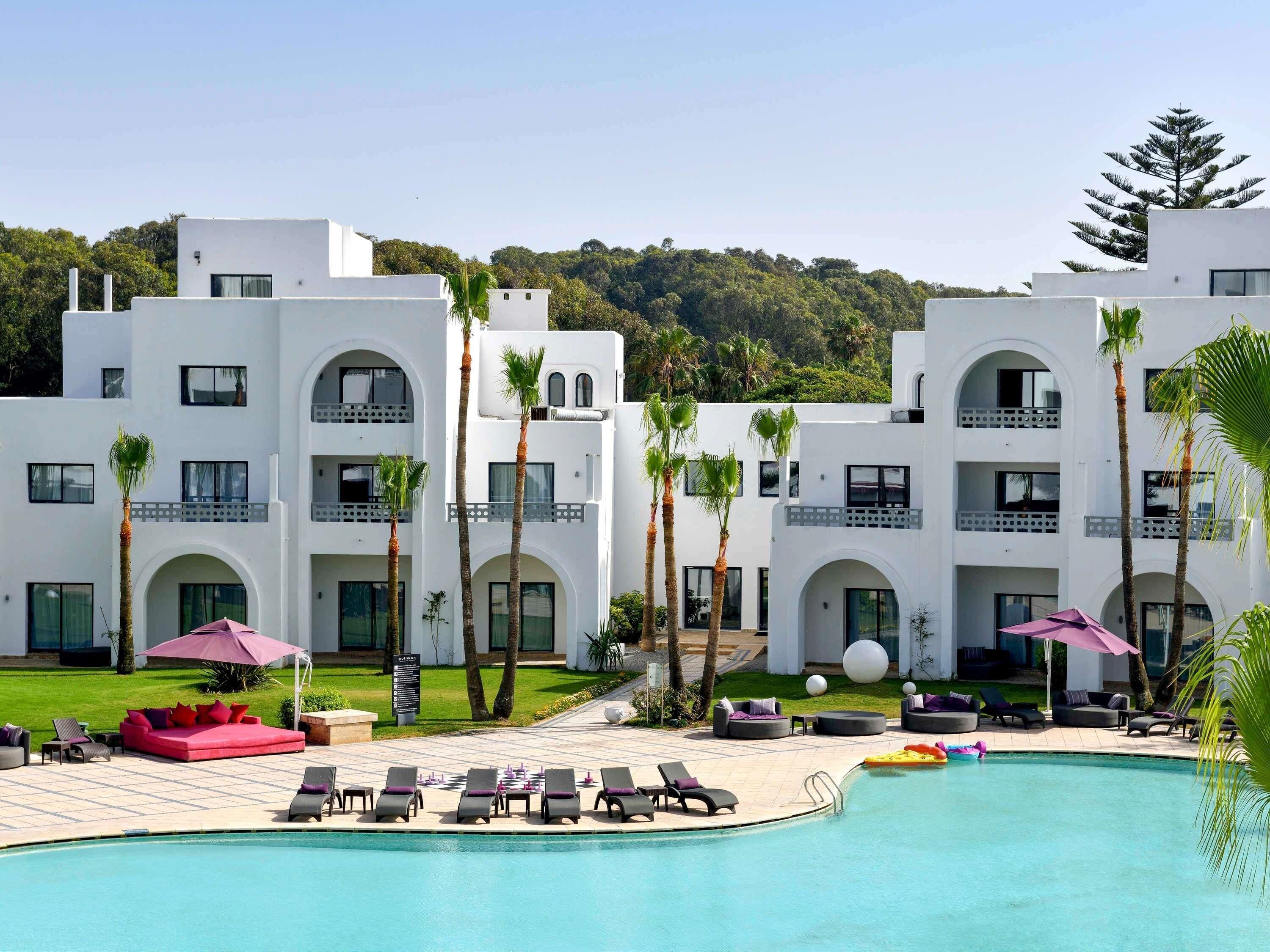 Een resort met een zwembad, ligbedden en palmbomen.