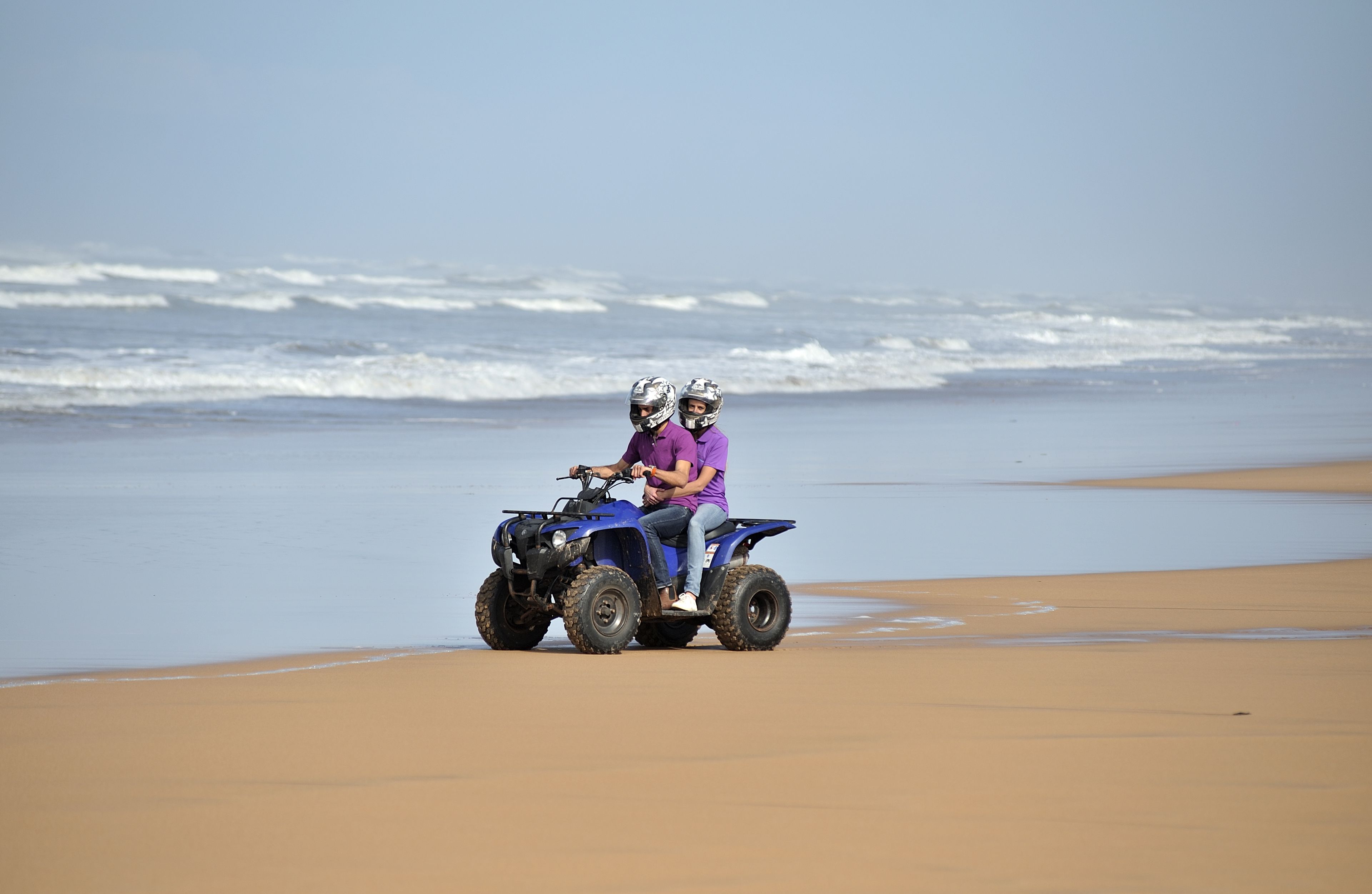 A beach with a blue ATV and two people riding it.