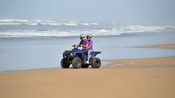 A beach with a blue ATV and two people riding it.