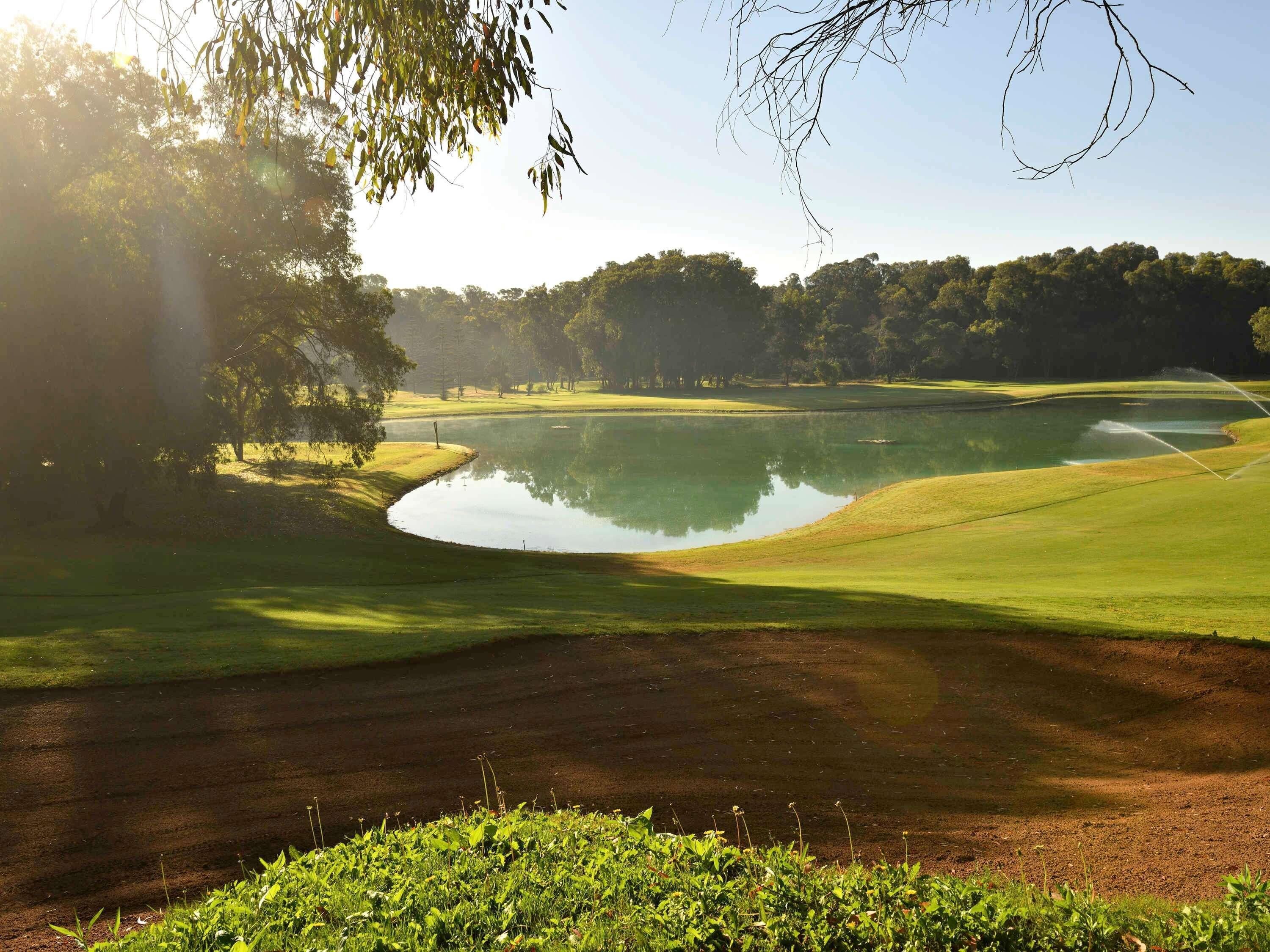 A golf course with a pond, trees, and a clear sky.