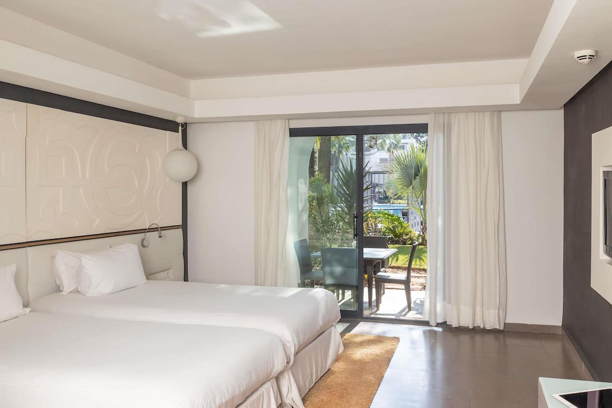Een hotelkamer met twee bedden, een groot raam met gordijnen, een zithoek met stoelen en een televisie aan de muur.