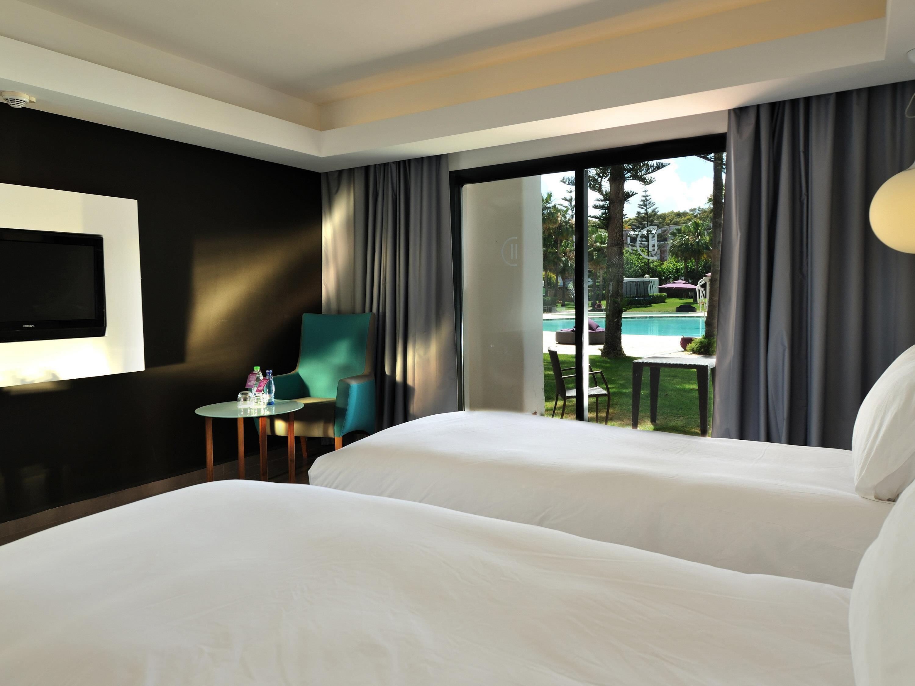 A hotel room with a bed, a TV, a small table with a chair, and a view of an outdoor pool.