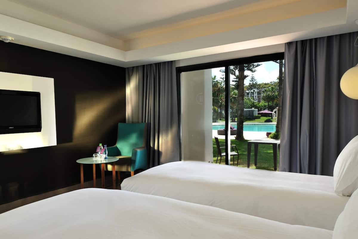 A hotel room with a bed, a TV, a small table with a chair, and a view of an outdoor pool.