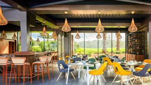 A modern dining area with high ceilings, exposed beams, and large windows offering a view of greenery.