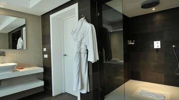A modern bathroom with a large mirror, a white bathtub, a glass-enclosed shower, and a white robe hanging on a hook.