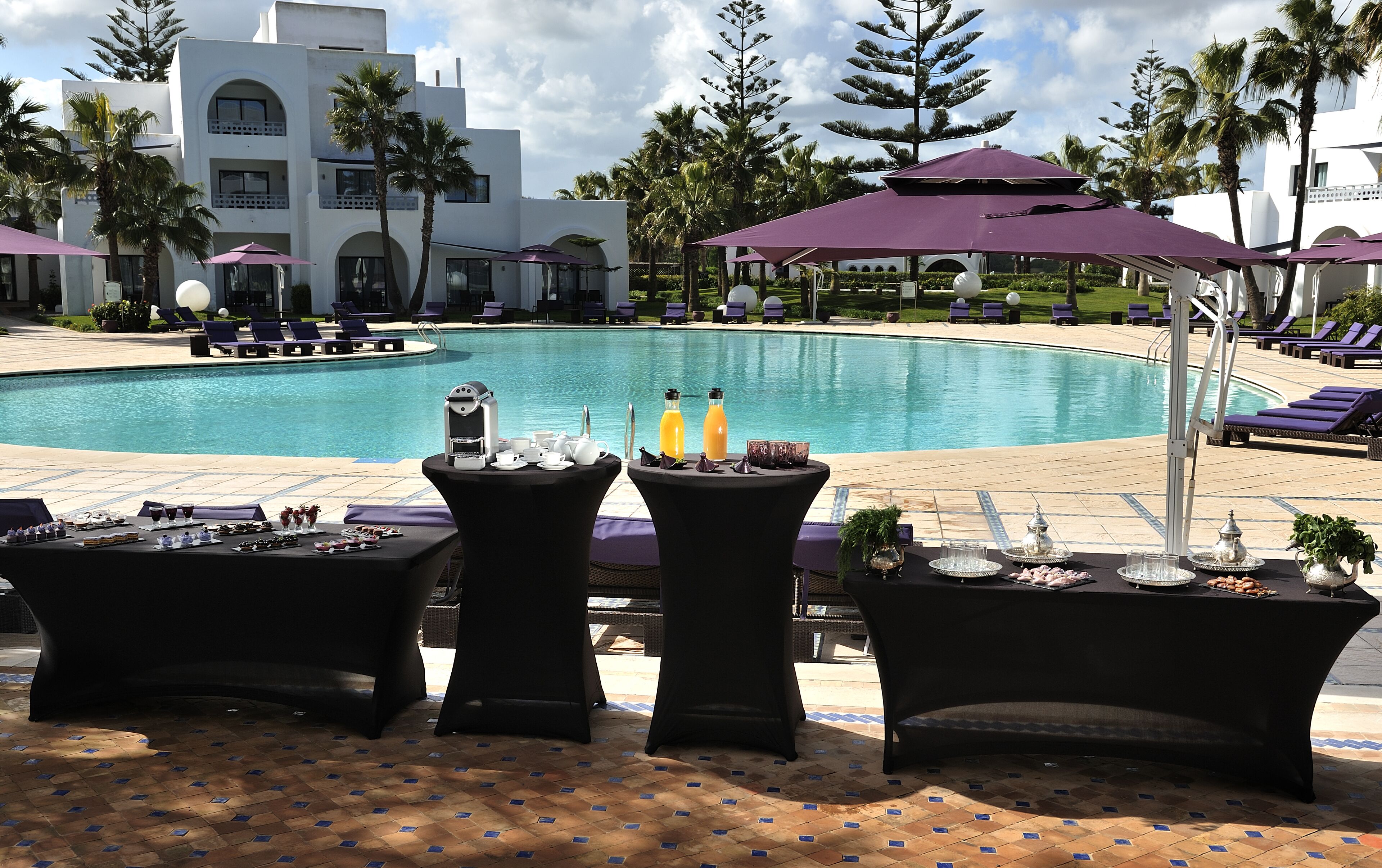 Zona junto a la piscina con sillones de descanso, una mesa con bebidas y vistas a la piscina.