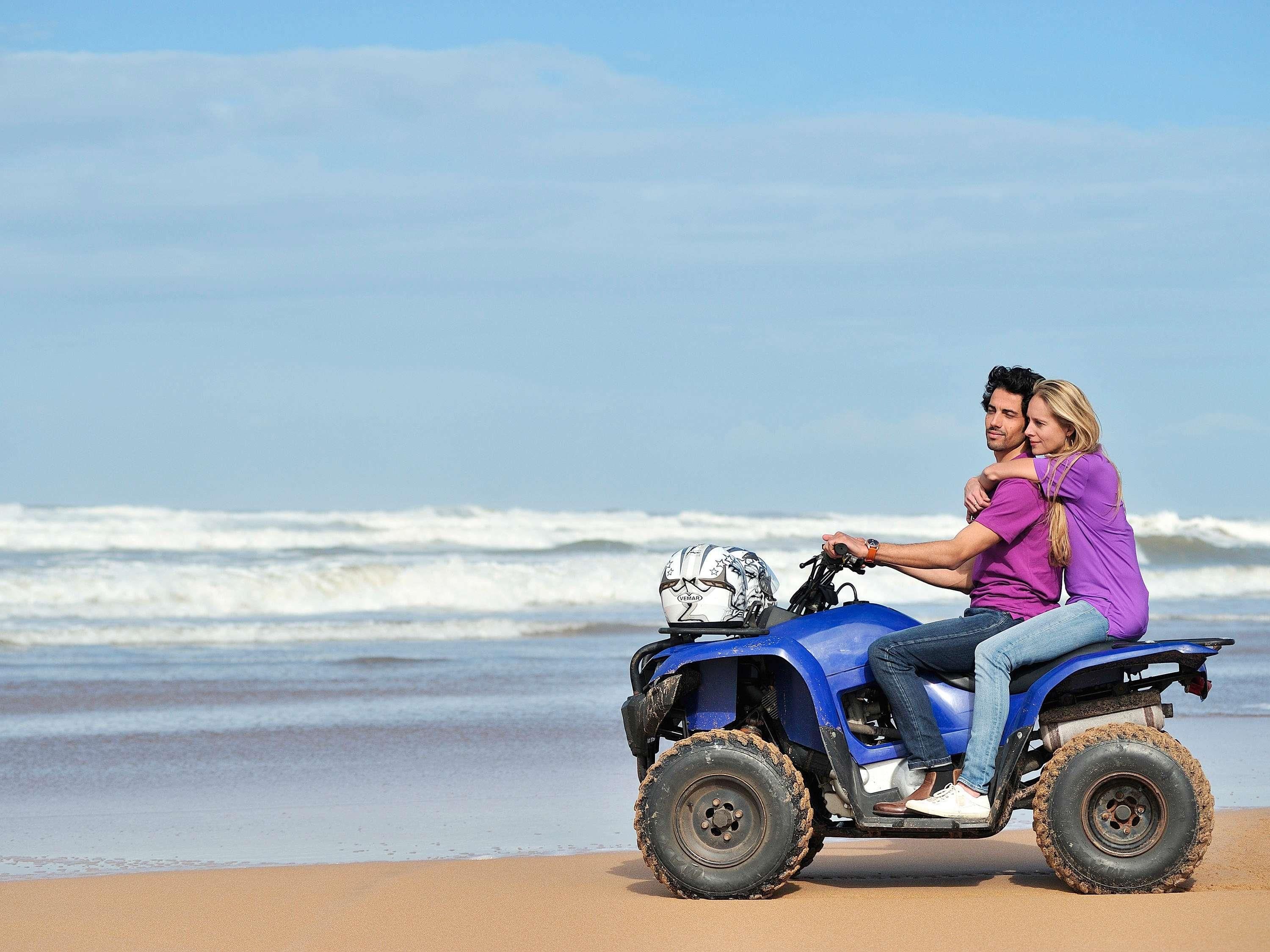 A person riding a blue ATV on a sandy beach with ocean waves in the background.