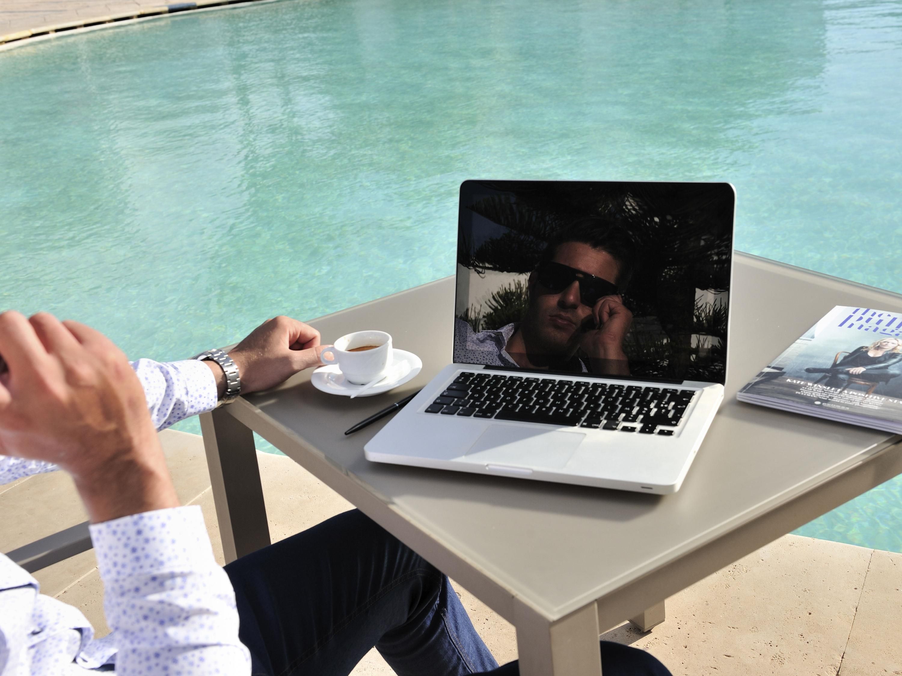 Un ordinateur portable est posé sur une table près d’une piscine, avec un magazine à côté.