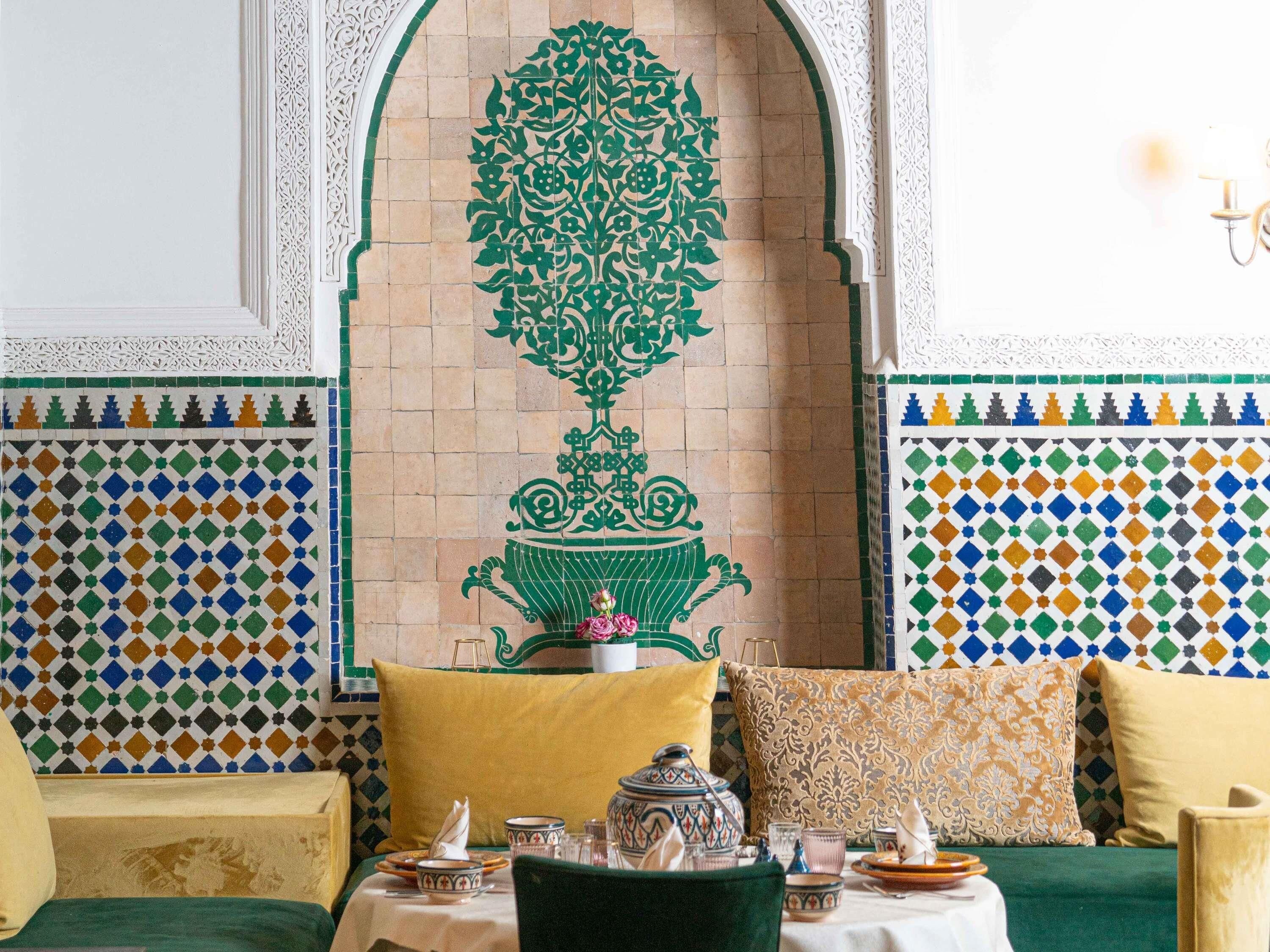 A dining area with a table set for two, a decorative wall with geometric tile patterns, and a green floral design above the door.