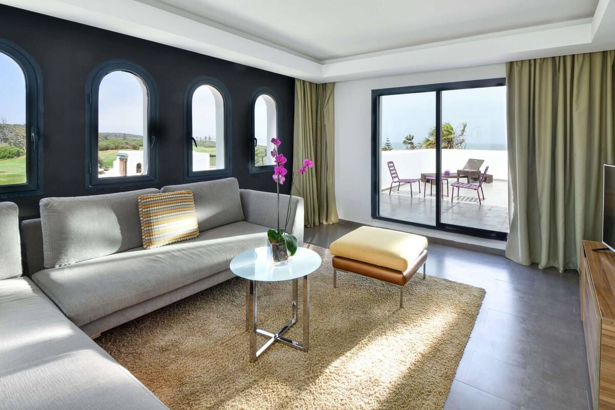 Een moderne woonkamer met een bank, een bijzettafeltje en uitzicht op een balkon met tuinmeubilair.