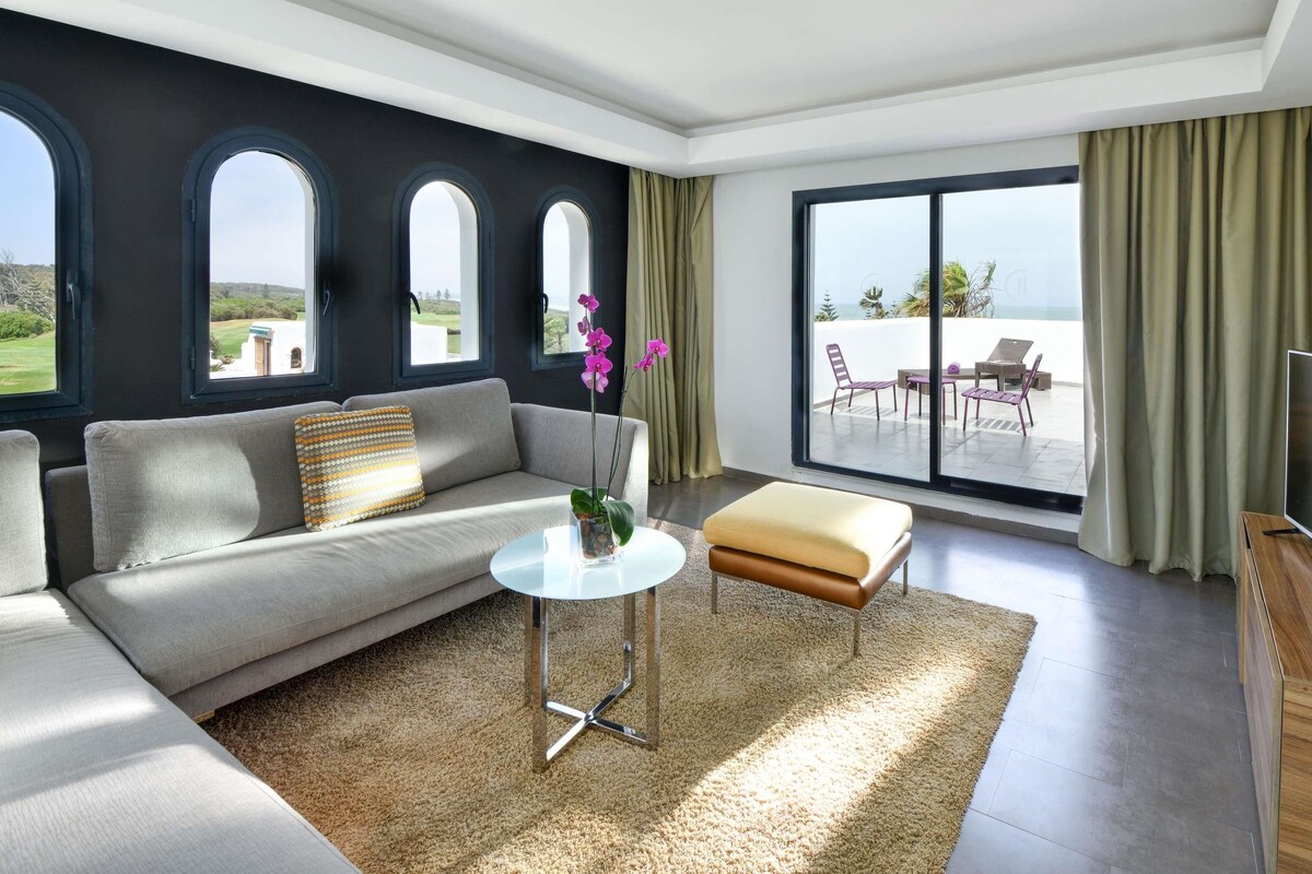Una sala de estar moderna con un sofá, una mesa de centro y vistas a un balcón con mobiliario exterior.