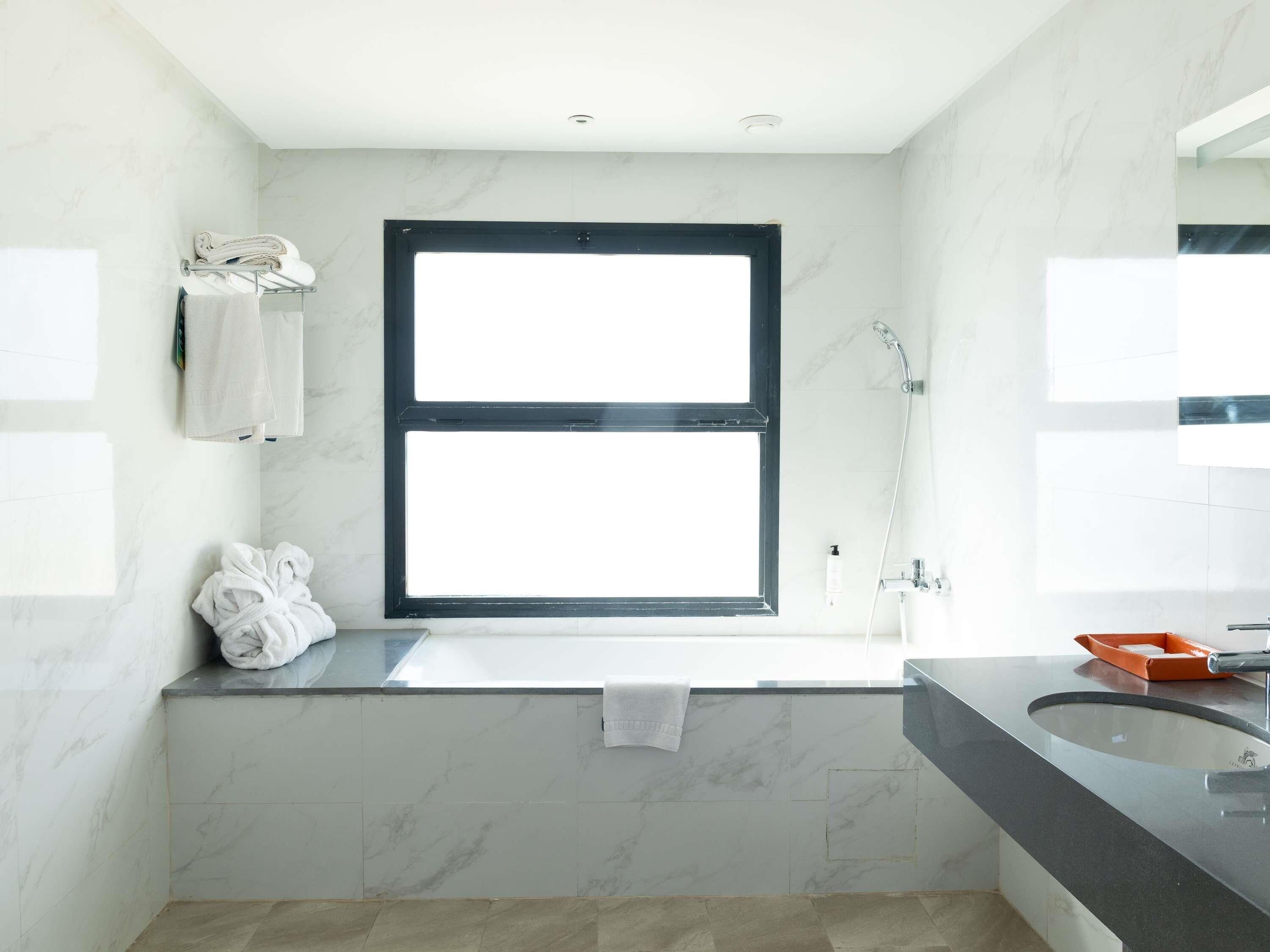 Une salle de bain moderne dotée d’une grande fenêtre, d’une baignoire, d’une douche et d’un lavabo.