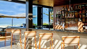 Eine Bar mit Meerblick, Barhocker und einer Flaschen- und Gläserauslage.