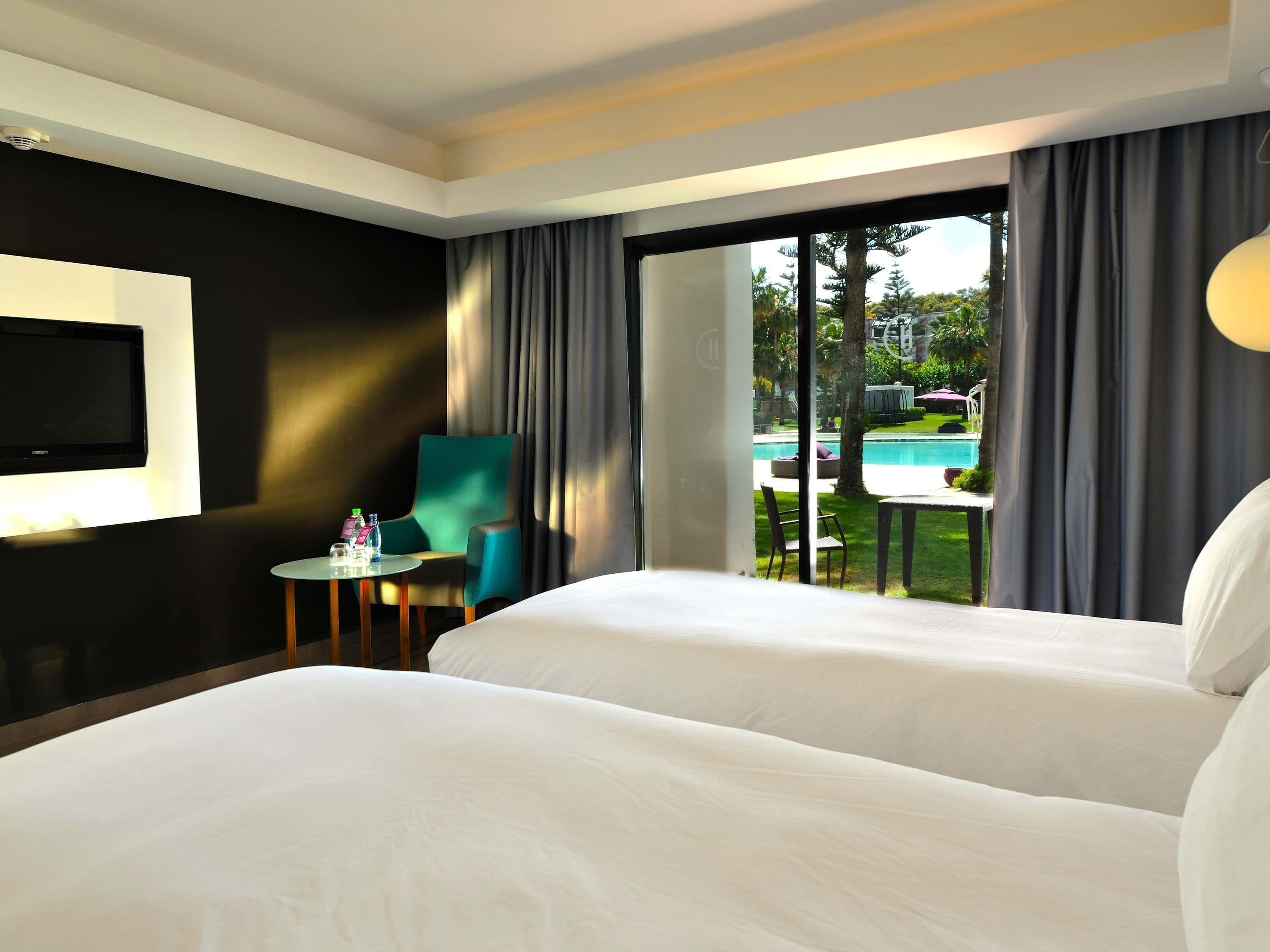 Ein Hotelzimmer mit Bett, Fernseher, Stuhl, Tisch und Blick auf einen Pool.
