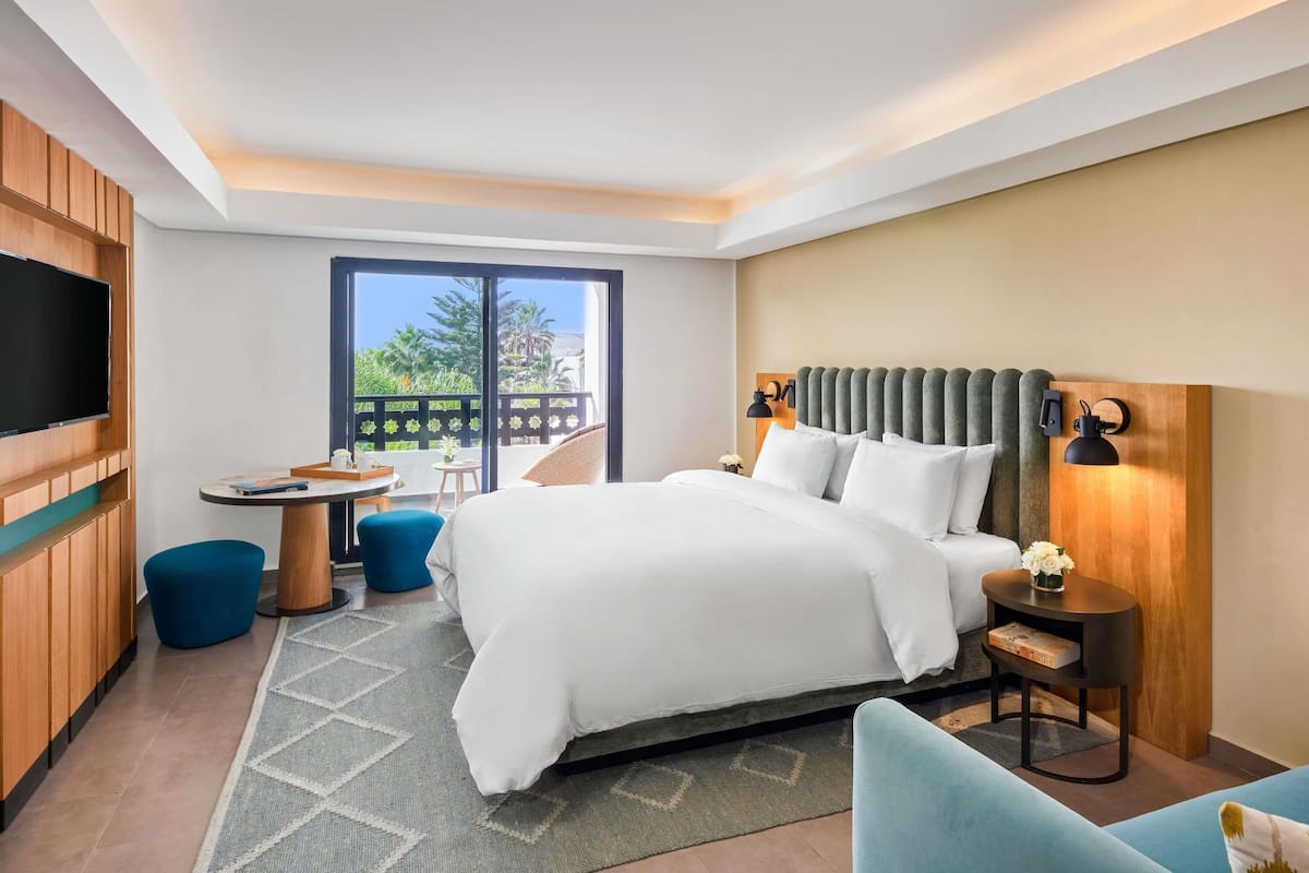Een hotelkamer met een groot bed, een televisie, een balkon met uitzicht en een bureau met een stoel.