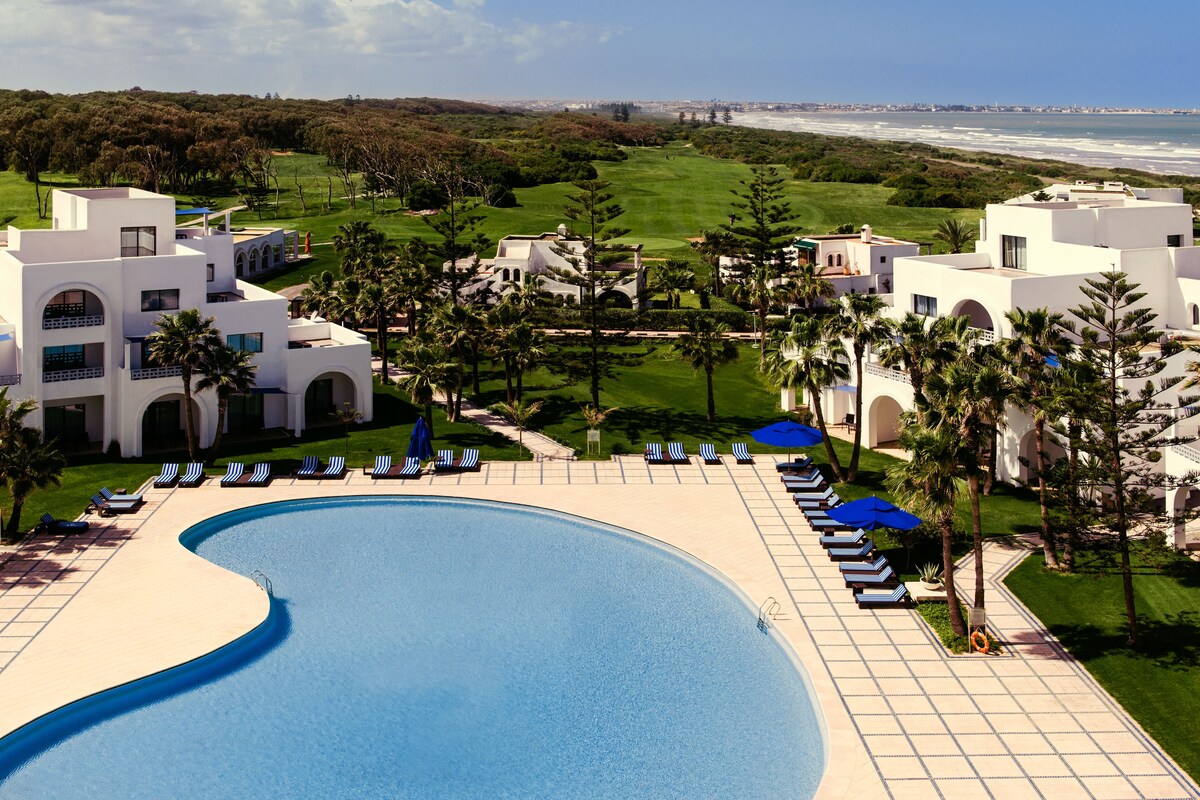Un resort con piscina, sillas de descanso y vista al océano.