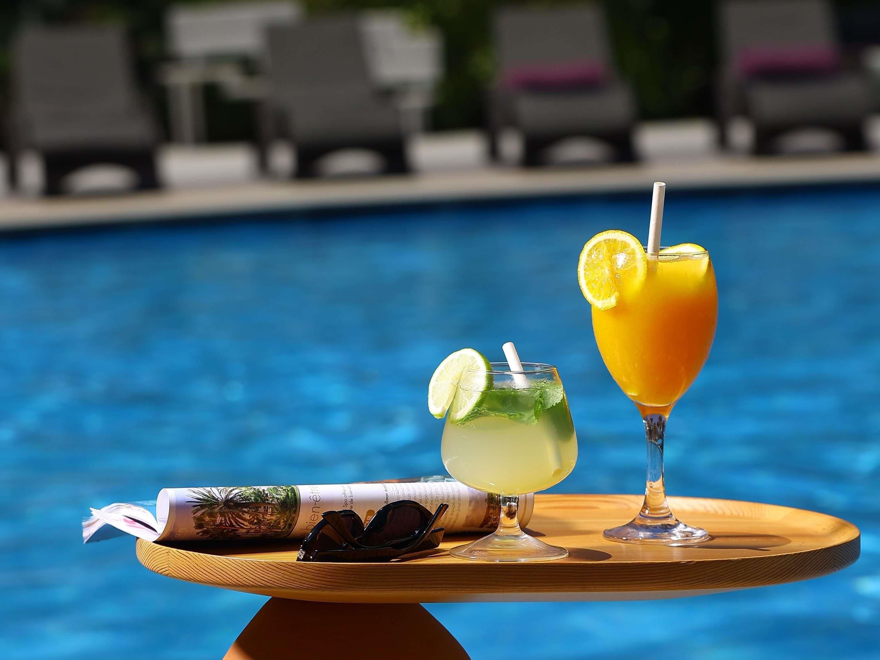 Una mesa junto a la piscina con una bebida, gafas de sol y una revista.