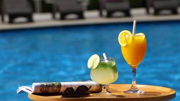 Una mesa junto a la piscina con una bebida, gafas de sol y una revista.
