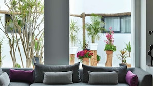 Een moderne woonkamer met een grijze bank, zwart-wit gestreepte kussens en een glazen salontafel. Er staan potplanten en er is uitzicht op het omliggende landschap door grote ramen.